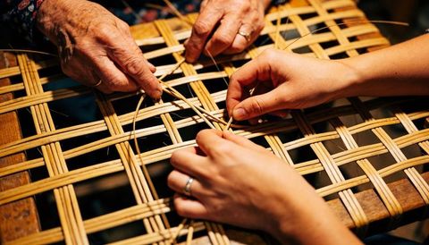 Senior and young hands weaving rattan lattice on wooden frame multigenerational craft lesson
