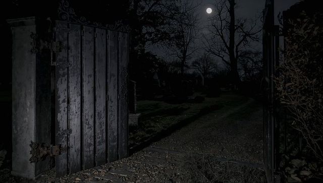 Eerie cemetery gate with full moon light on gravel path