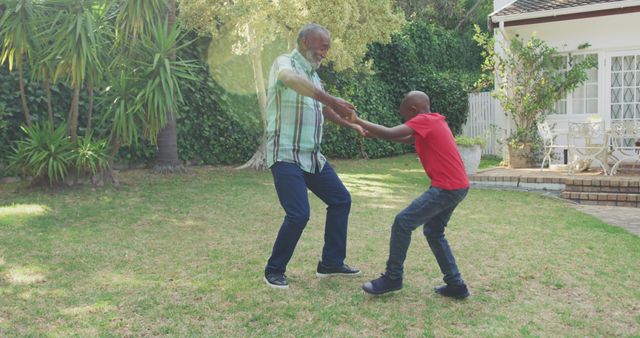 Happy african american grandfather and grandson dancing in garden. Lifestyle, domestic life, family, and togetherness.