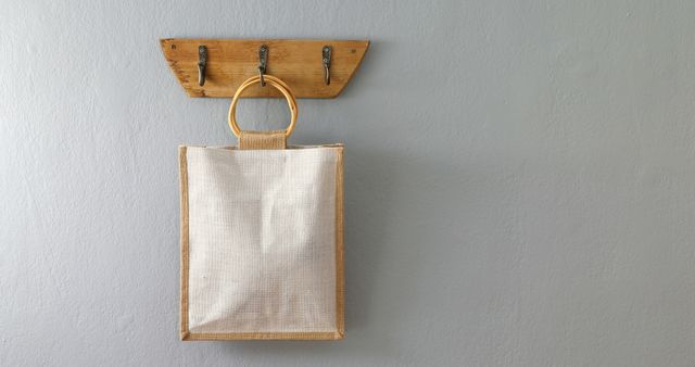 Eco-friendly tote bag hangs on a rustic wooden hook attached to a gray wall, highlighting minimalistic and sustainable living. Useful for articles or advertisements related to sustainability, home organization, eco-living, and stylish storage solutions.