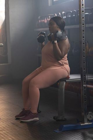 African american woman lifting dumbbells wearing peach activewear focusing on strength