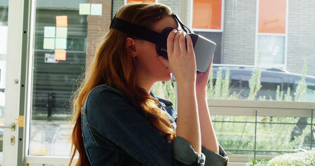 Young woman engaging with a virtual reality headset in an office environment. Ideal for representing modern technology use, innovation, and digital exploration. Perfect for tech blogs, VR content, and articles on immersive technology.