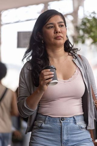 Woman walking with coffee through busy transit concourse wearing pink camisole and denim