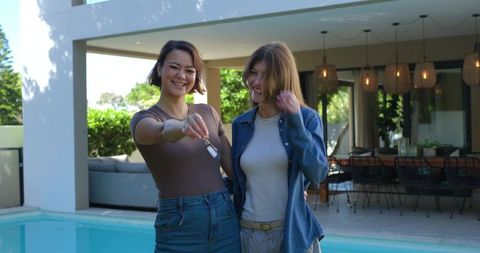 Young women holding house keys by pool celebrating new home on modern patio