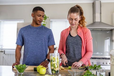 Couple preparing green smoothie on kitchen island using personal blender