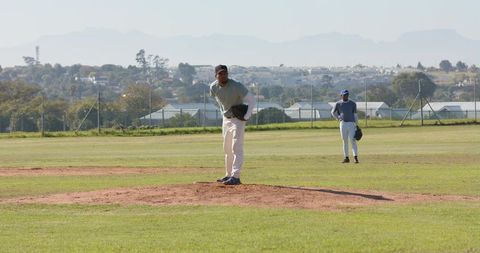 Pitcher preparing throw on mound with teammate standing in outfield on baseball field