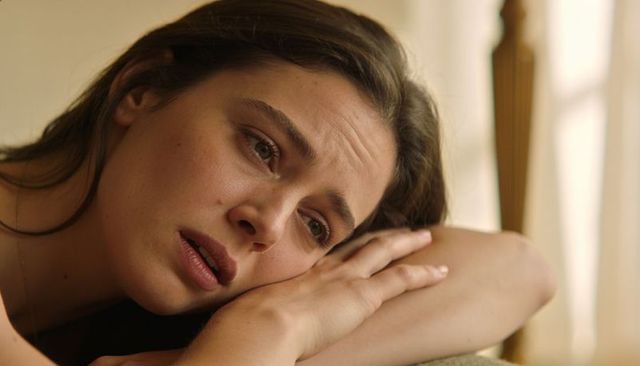 Pensive young woman resting on arm by window, intimate close-up portrait for wellbeing