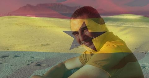 Man sitting on sand dunes at sunset with ghana flag overlay conveying patriotism