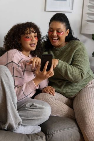 Mother and teen sharing cozy skincare moment on couch with under-eye patches