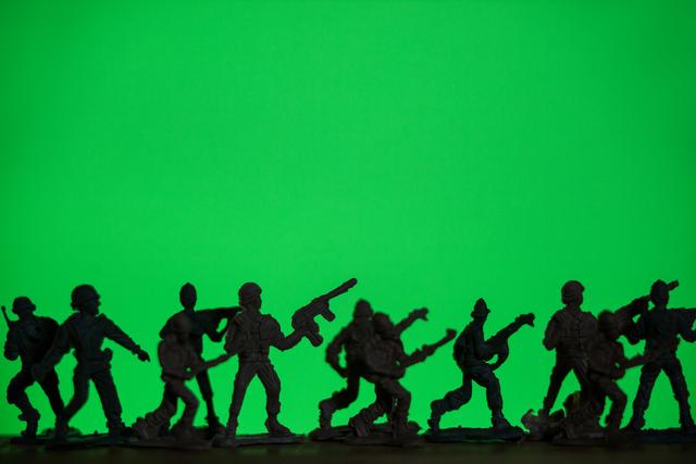 Silhouetted toy soldiers stand in a line against a vibrant green background, creating a dramatic and playful scene. Ideal for use in articles or advertisements related to childhood, playtime, military strategy games, or toy collections. Can also be used in educational materials about history or military tactics.
