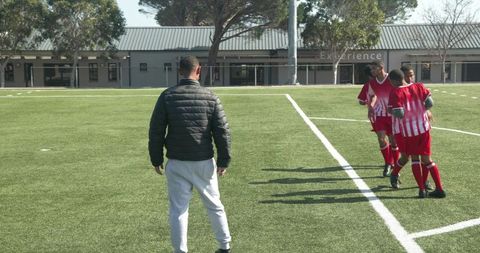 Soccer coach instructing team on field in sunny day