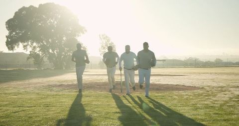 Cricket teammates running toward camera at sunrise carrying bat past wicket stumps cinematic
