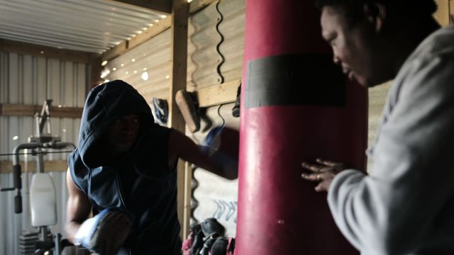 Boxer in sportswear training with coach, punching bag in gym. Good for fitness articles, sports training programs, athlete motivation content.