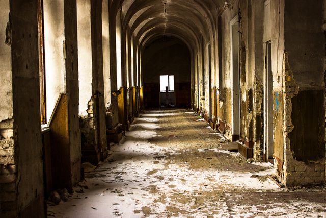 Depicts an abandoned corridor inside a deteriorating building, showing signs of decay, including peeling paint and debris-lined floors. Useful for projects about urban exploration, abandoned places, historical documentation, or backgrounds for horror stories.
