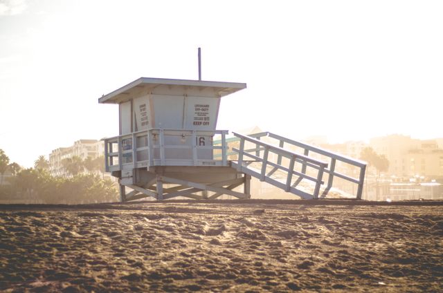 Beach lifeguard tower bathed in sunset light on a sandy shore. Ideal for depicting coastal life, summer vacations, and serene days at the beach. Perfect for travel brochures, vacation promotions, and beach lifestyle blogs.