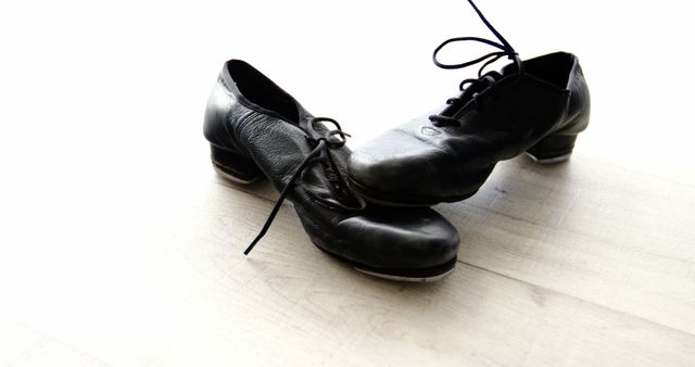 A pair of black tap shoes rests on a wooden floor, with copy space. Tap shoes like these are essential for dancers specializing in tap dancing, a performance art that creates rhythmic sounds through the movement of the feet.