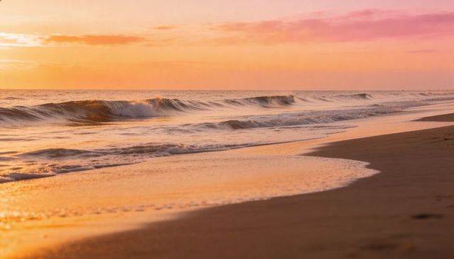 Rolling waves reflecting golden pastel sky on serene sandy shore at golden hour