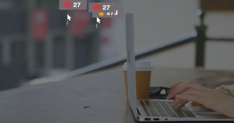 Woman typing on laptop at outdoor cafe with coffee cup, glasses and notification alerts