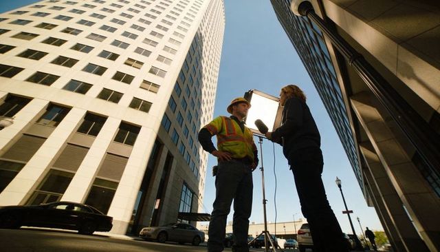 Urban on-site interview between reporter and construction worker with boom mic
