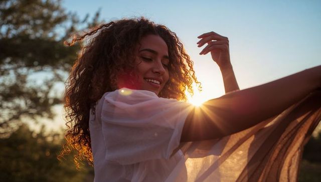 Basking in golden sunset, smiling woman holding sheer shawl and showing ring outdoors