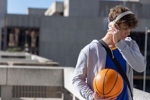 Teen basketball player listening to headphones on urban rooftop holding ball