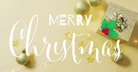 Merry christmas handwritten script on gold holiday flatlay with gift box and baubles