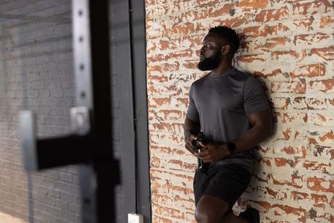 African american athlete leaning on brick wall holding shaker post-workout industrial gym