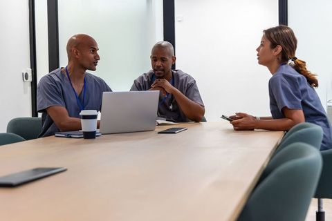 Diverse medical team collaborating over laptop and notes in conference room for patient care plannin