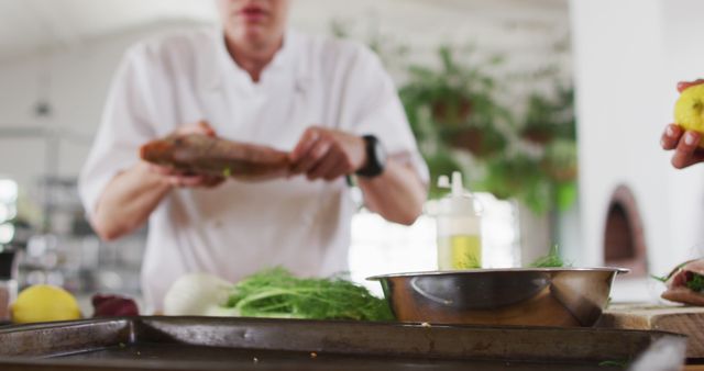 Chef preparing fish in a modern kitchen environment. Fresh vegetables like fennel and lemons are visible. Ideal for articles or blogs on gourmet cooking, recipes, professional culinary training, healthy eating, food preparation, or kitchen scenes.