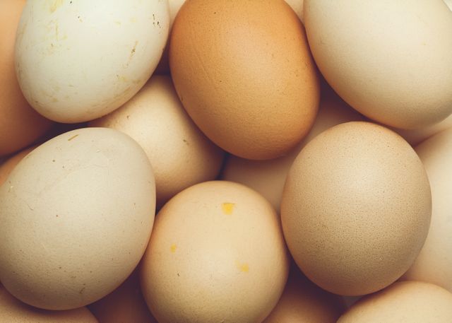 Close-up view of a pile of fresh farm eggs of various shades of brown and white. Ideal for use in advertisements for organic food products, articles about farm-to-table cuisine, or blog posts focusing on healthy eating and protein sources.