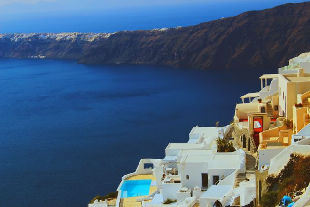 Whitewashed buildings perched on cliffs of Santorini island with stunning views of caldera and Aegean Sea below. Popular tourist destination, ideal for travel promotions, vacation brochures, luxury resort marketing, or illustrating scenic coastal views. Emphasis on Mediterranean architecture and natural beauty.
