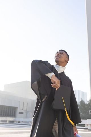 African american graduate celebrating on rooftop with mortarboard and yellow tassel