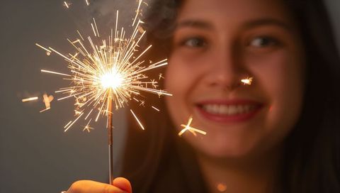 Smiling woman holding lit sparkler closeup celebrating indoor party warm golden glow