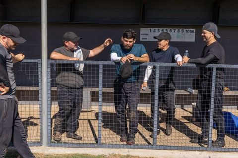 Men's baseball team leaning on dugout fence taking water break during sunny amateur game