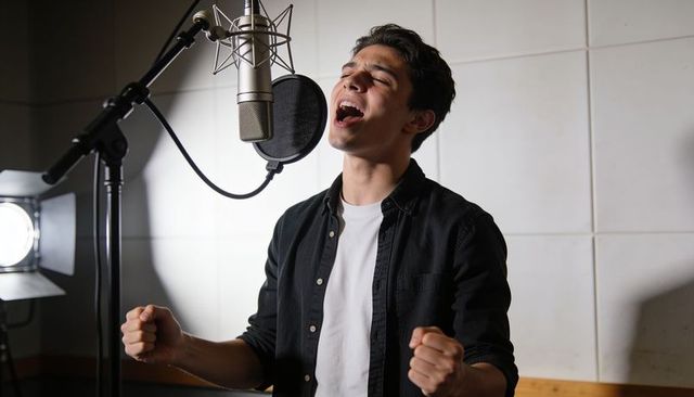 Male vocalist singing passionate take in professional recording studio with condenser mic
