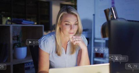 Mature professional woman working late on laptop with analytics overlays and desk lamp