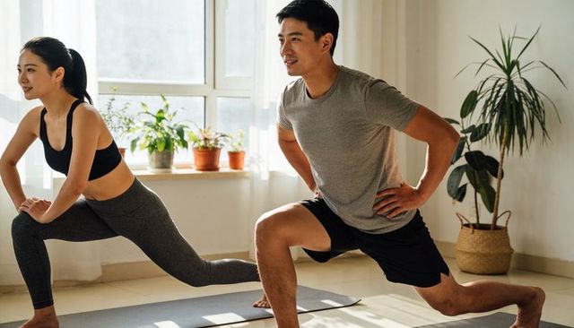 Young couple doing forward lunges in sunlit apartment, at-home workout, wellness lifestyle