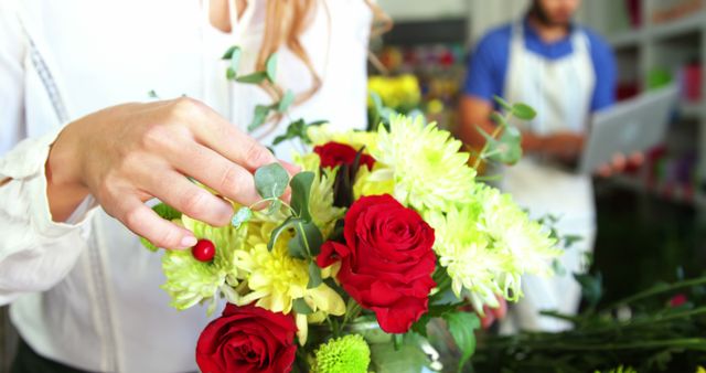 Image depicting a florist arranging a beautiful bouquet with red roses and white flowers. Such images are ideal for use in articles about flower shops, floral arrangement tips, florist careers, and decoration ideas. Perfect for promoting small businesses, events, and nature's beauty through floral displays.