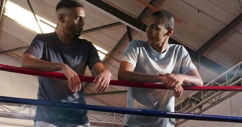 Two male boxers leaning on ring ropes talking after sparring and training