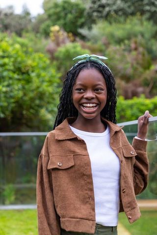 Smiling african american teen girl with braids on balcony enjoying lush garden lifestyle