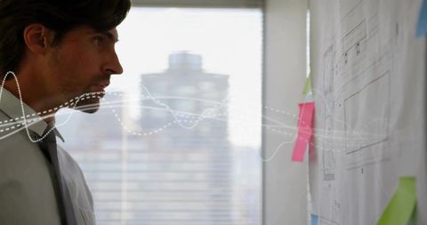 Engineer studying architectural plans with sticky notes and waveform overlay in office