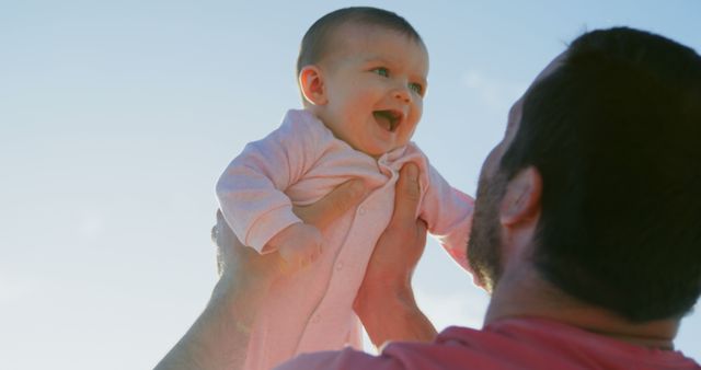 Caucasian father holding happy baby above his head against sunny blue sky, copy space - Download Free Stock Photos Pikwizard.com