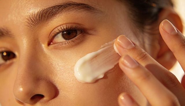 Applying moisturizer on cheek, asian woman creating dewy glowing skin with gentle fingers