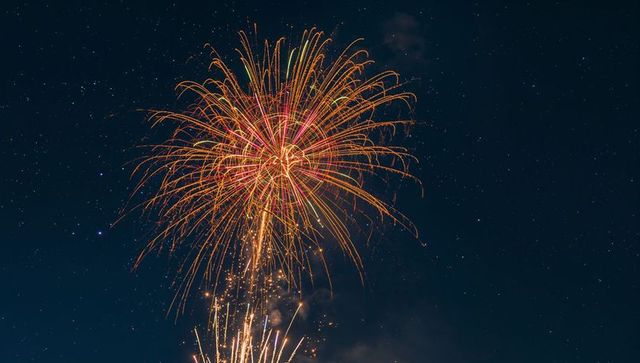 Lighting chrysanthemum firework burst sending golden-red spark trails across night sky