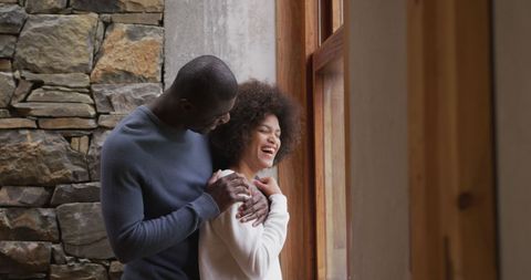 Happy Multiracial Couple Embracing and Laughing by Window