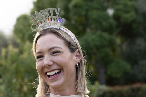 Laughing woman wearing merry christmas headband celebrating outdoors in garden portrait