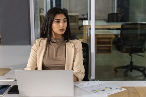 Indian businesswoman reviewing charts at laptop in modern glass office