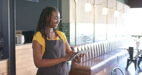 Smiling cafe server using tablet in modern coffeehouse with leather banquette