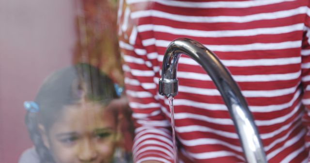 A young girl is reflected in a water tap, highlighting the importance of clean water and sanitation for children. Her gaze seems focused on the water droplet, symbolizing the preciousness of this resource.