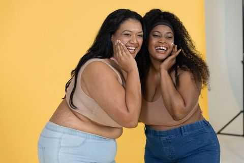 Joyful diverse plus-size friends laughing and posing in studio with yellow backdrop
